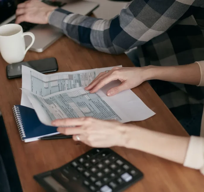Main d'une personne signant un document administratif professionnel avec calculatrice et papiers comptables sur le burea Main d'une personne signant un document administratif professionnel avec calculatrice et papiers comptables sur le burea