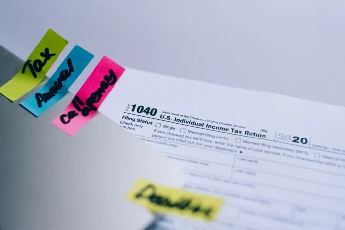 Mains tenant une tablette affichant un formulaire de correction d'impôts sur un bureau avec documents Mains tenant une tablette affichant un formulaire de correction d'impôts sur un bureau avec documents