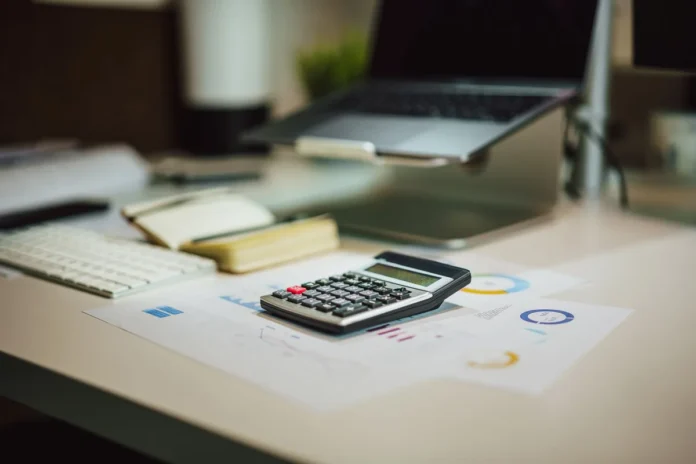 Mains tenant un acte immobilier et une calculatrice sur le bureau d'un notaire Mains tenant un acte immobilier et une calculatrice sur le bureau d'un notaire