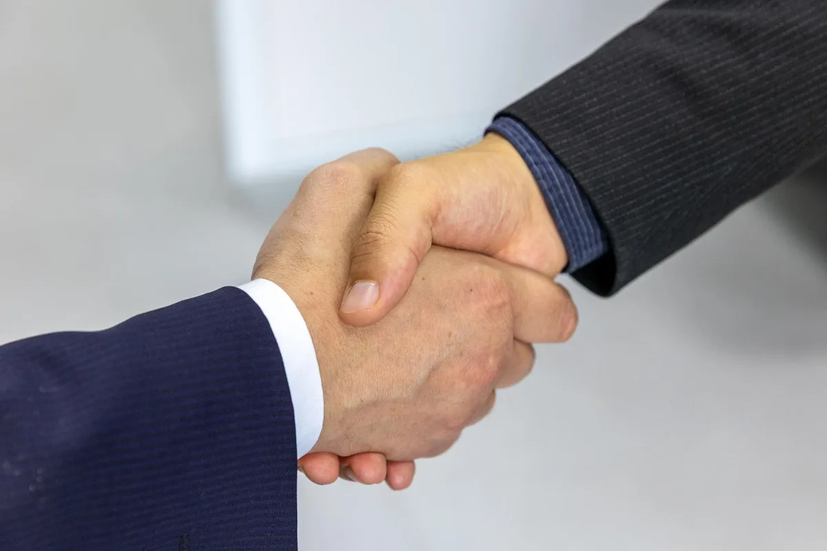 Deux professionnels se serrent la main lors d'une réunion d'affaires dans un bureau moderne.