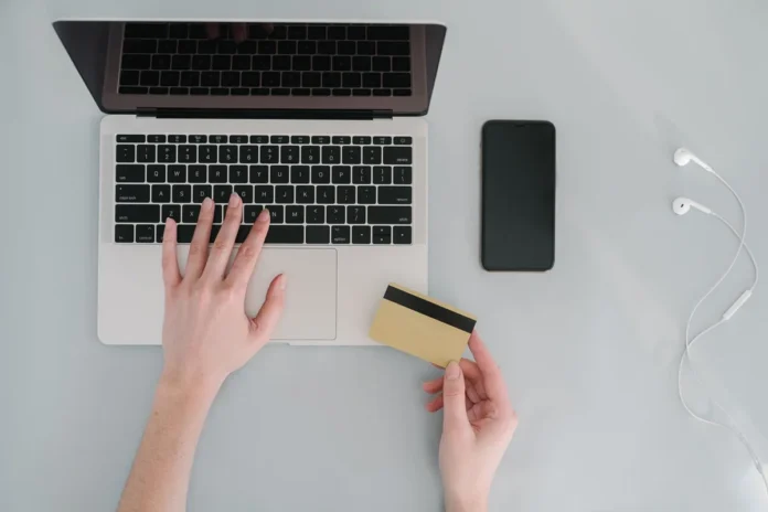 Mains tenant une carte bancaire et un smartphone au-dessus d'un ordinateur portable affichant un tableau de bord bancair Mains tenant une carte bancaire et un smartphone au-dessus d'un ordinateur portable affichant un tableau de bord bancair