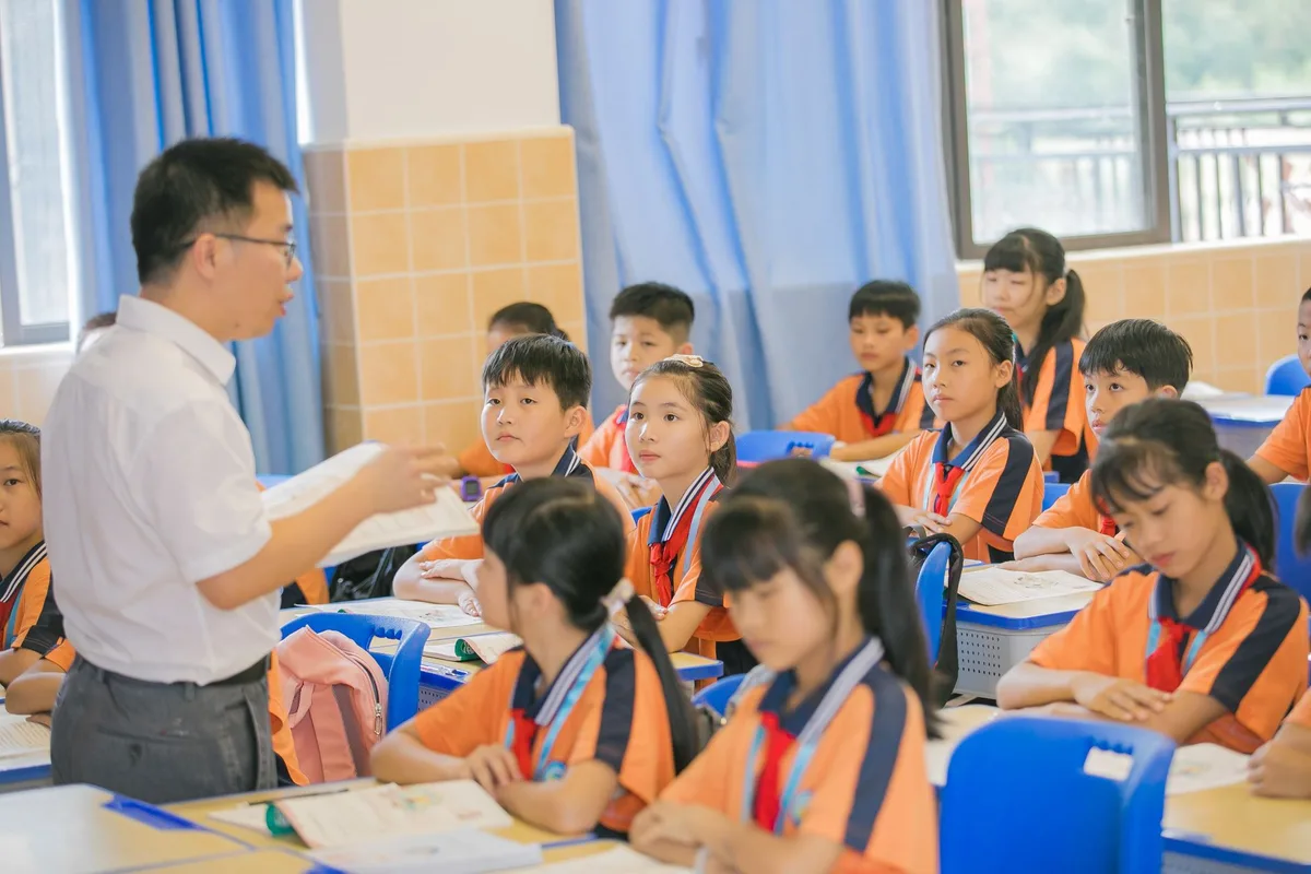 Une enseignante observe attentivement des enfants assis en classe, créant un environnement d'apprentissage bienveillant.
