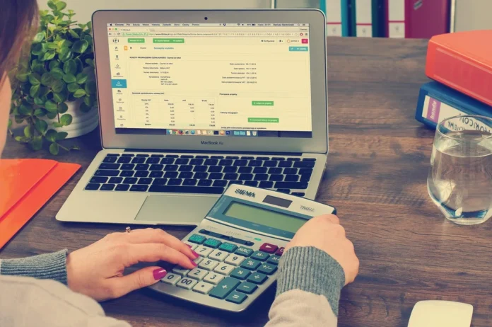 Mains tenant un chèque annulé au-dessus d'un grand livre comptable avec stylo et calculatrice Mains tenant un chèque annulé au-dessus d'un grand livre comptable avec stylo et calculatrice