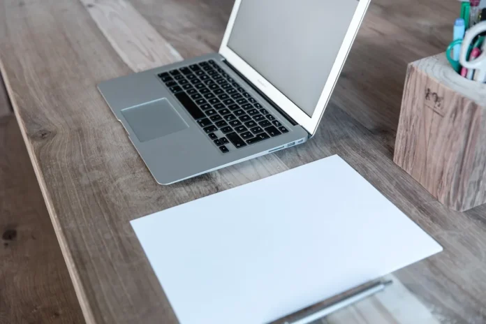 Bureau près d'une fenêtre en journée avec ordinateur portable et carnet, mains prenant des notes Bureau près d'une fenêtre en journée avec ordinateur portable et carnet, mains prenant des notes