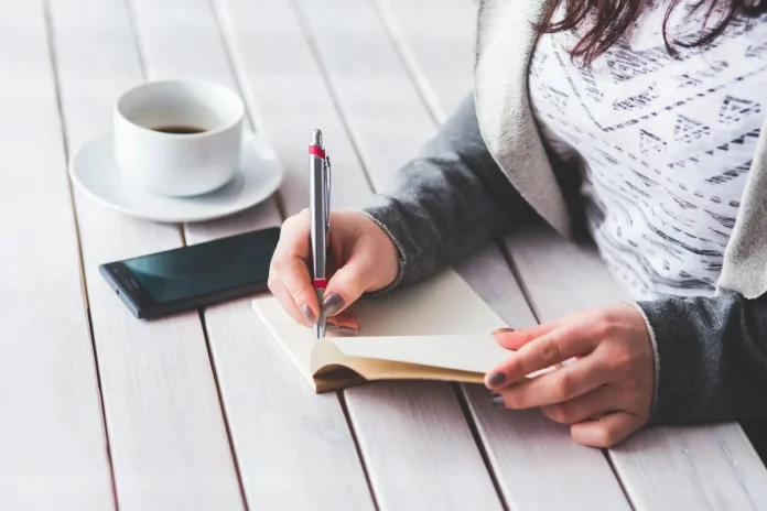 Personne anonyme tapant sur un ordinateur portable avec notes et carnet sur une table en plein jour Personne anonyme tapant sur un ordinateur portable avec notes et carnet sur une table en plein jour